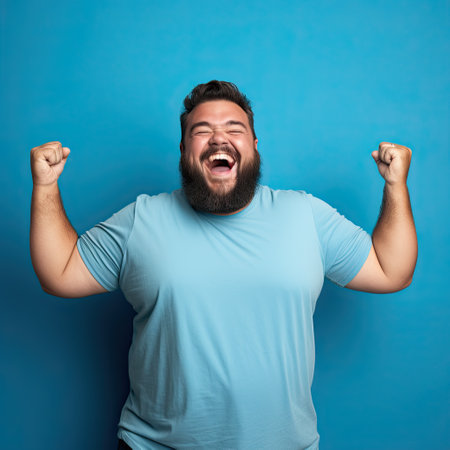 Excited fat man celebrating success. Happy plus size bearded man on blue background.の素材