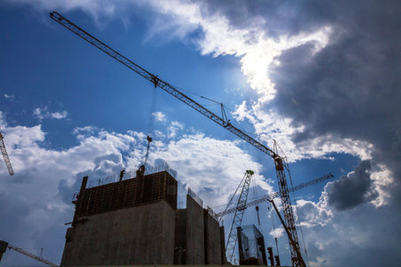 Construction site with workers and tower cranes against dramatic cloudy sky. Industrial background of construction process, urban development and architecture.の写真素材