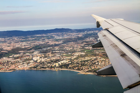 View from airplane window with visible wing flying over coastal city, sea and mountains. Travel,...