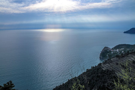 A picturesque seascape with sunlight breaking through the clouds over a calm ocean horizon, a...