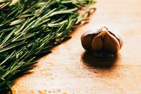 bundle of sprigs of rosemary and garlic on a wooden light background.の写真素材
