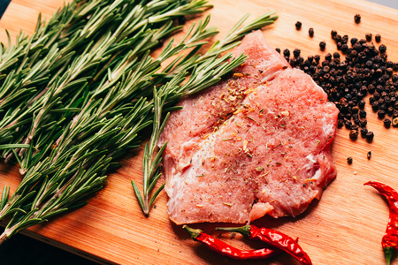 raw meat, sprig of rosemary and red hot pepper on a wooden light background.の写真素材