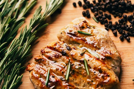grilled meat, sprig of rosemary and red hot pepper on a wooden light background.の写真素材