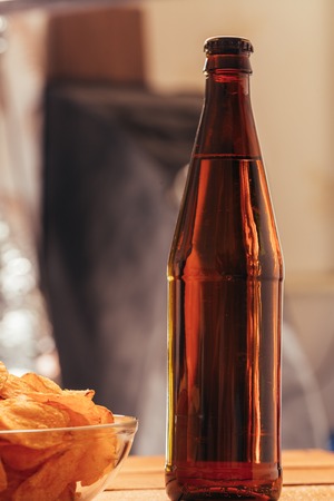 brown beer bottle with a bowl of chips on a blurred background.の写真素材