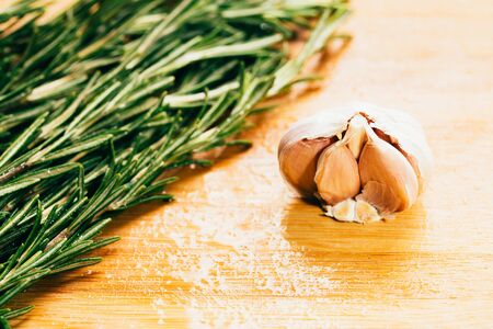 bundle of sprigs of rosemary and garlic on a wooden light background.の写真素材