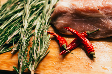 raw meat, sprig of rosemary and red hot pepper on a wooden light background.の写真素材