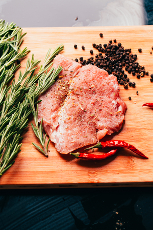 raw meat, sprig of rosemary and red hot pepper on a wooden light background.の写真素材