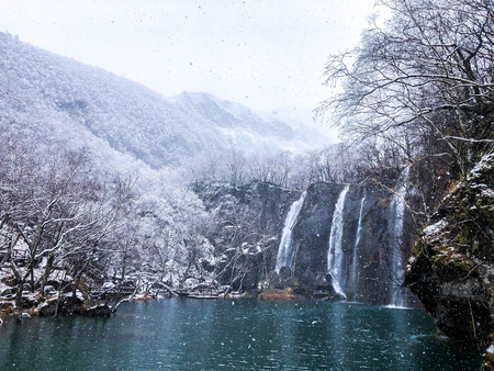Winter waterfall among snow-capped mountains and forestsの写真素材