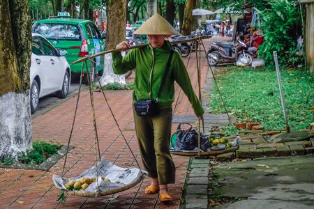 Hue, Vietnam - January 30, 2018: A woman carries a rocker with baskets of food for sale.のeditorial素材