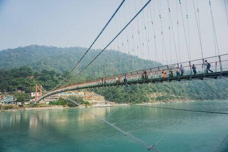 Rishikesh, India - November 3, 2017: People cross the Ganges River on a pedestrian suspension...