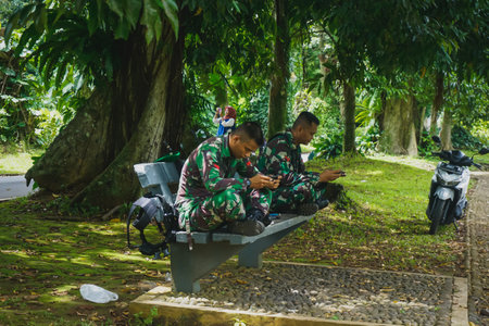 Bogor, Indonesia - February 2, 2019: Indonesian military stuck in phones on a bench in a parkのeditorial素材