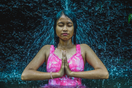 Indonesian girl meditating under a waterfallの写真素材