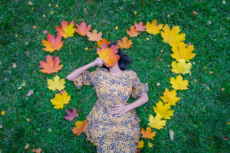Girl in an autumn heart made of yellow leaves in a parkの写真素材