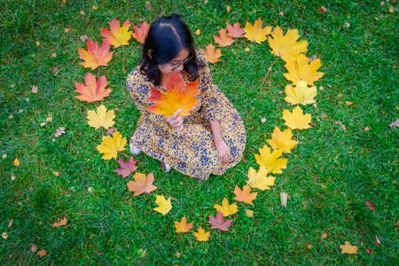 Girl in an autumn heart made of yellow leaves in a park