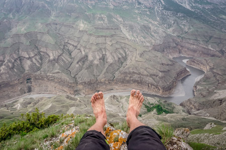 A man sits with his legs dangling over the Sulak canyonの写真素材