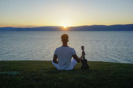 Guy in white clothes with ukulele at sunsetの写真素材
