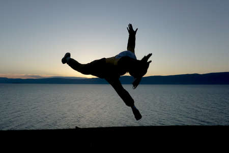 Silhouette of a man doing acrobatic exercises in nature in Baikal