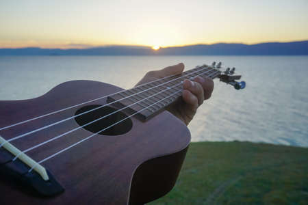 Ukulele in the hand of a man at sunsetの写真素材