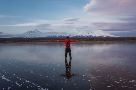 A Man on a Frozen Lake with a View of Kamchatka Volcanoes at sunsetの写真素材