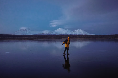 A Man on a Frozen Lake with a View of Kamchatka Volcanoes at sunsetの写真素材