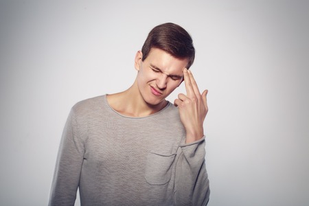 Frustration and despair. Close-up of handsome young man gesturing hand gun and keeping eyes closed...