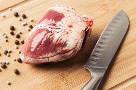 Raw sheep heart wooden board for cutting meat with knife and spices.の写真素材