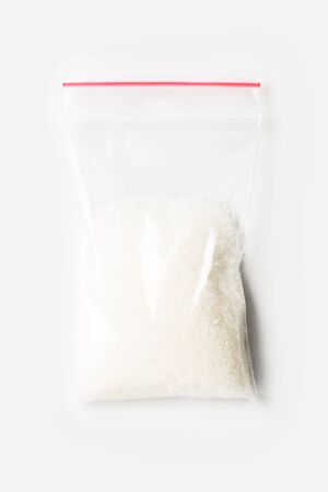 Plastic transparent zipper bag with half Granulated sugar isolated on white, Vacuum package mockup with red clip. Conceptの写真素材
