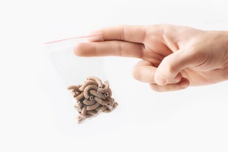 Hand holding Plastic transparent zipper bag with half wholegrain raw pasta isolated on white, Vacuum package mockup with red clip. Conceptの写真素材