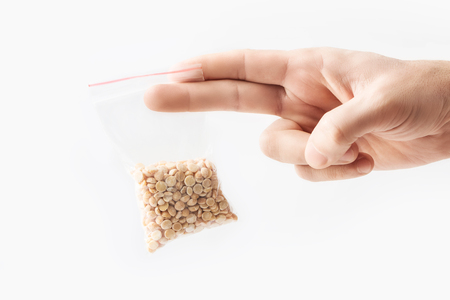 Hand holding Plastic transparent zipper bag with half raw organic split peas isolated on white, Vacuum package mockup with red clip. Concept.の写真素材