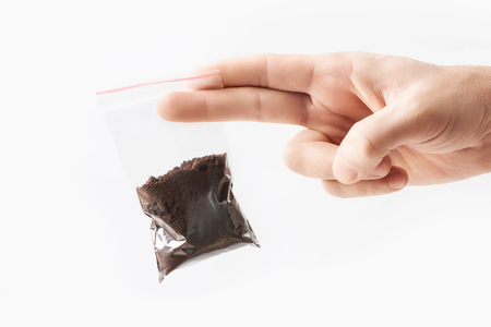 Hand holding Plastic transparent zipper bag with half Brewed coffee powder isolated on white, Vacuum package mockup with red clip. Conceptの写真素材