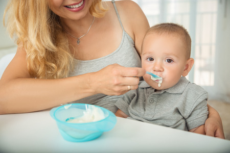 Mom feeds her little son porridge with a spoon. A balanced breakfast of porridge for the younger organism is a small child. Breakfast is full of vitamin and cereal for a little boy. Family breakfastの写真素材