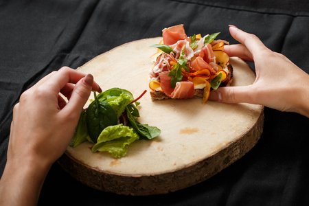 Close up sandwich with jamon and salad on board. Womans hand holding folk and knife. Sandwich with jamon and apple, salad. Delicious lunch. Serving dishes concept. Restaurant food conceptの写真素材