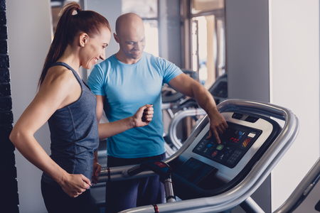 Personal training with a trainer on a treadmill. The trainer controls the correctness of the exercise when using a treadmill for cardio. Control coach in the gym. Athletic jogging with a trainerの写真素材