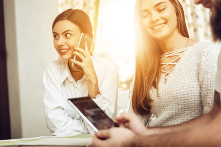 Group of Smiling Business People Working in Cafe. Smiling girl talking on a mobile phone against the background of a happy man and woman looking at a mobile phone. The concept of business people.の写真素材
