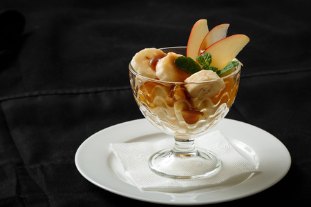 Close up ice cream dessert banana apple in glass. Fruit dessert with banana and apple is poured with jam in a glass on a white plate. The concept of culinary business and restaurant business.の写真素材