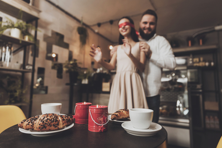 Beautiful girl with red ribbon on the eyes. A young bearded man arranges a surprise romantic dinner for his beloved girl in honor of the celebration of Valentine Day. Romantic dinner in a cafeの写真素材