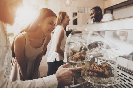 A smiling bearded man and a beautiful girl standing by the window choose fresh pastries. Against the background of young girl makes an order with a man barista. The concept of the restaurant businessの写真素材