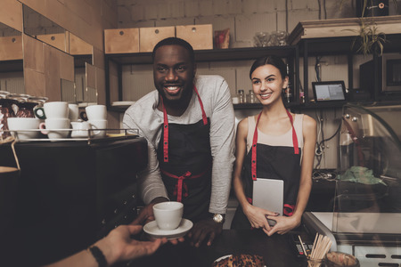 Team of male and female barista service customer. Afro-American barista male and beautiful smiling...