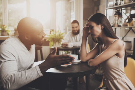 Young couple men and women find out the relationship. Young African American man and beautiful girl find out the relationship while sitting at a table in a cafe. Gackground of a young bearded manの写真素材