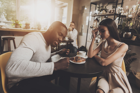 Young couple men and women find out the relationship. Young African American man and beautiful girl find out the relationship while sitting at a table in a cafe. Gackground of a young bearded manの写真素材