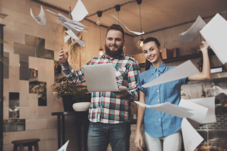 Young people rejoice at successful completion. A happy bearded man and a beautiful smiling girl scatter text documents to complete productive work. Business people conceptの写真素材