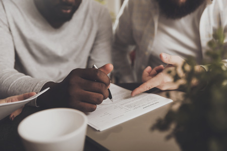 Young African American man signs documents. An international group of people signs working papers...