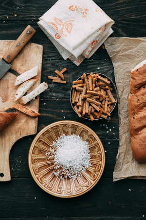 Loaf and crackers with salt on a black wooden background, with the fabric in the composition. Spices and sliced breadの写真素材