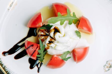 Restaurant dish on a wooden background with vegetables. Burrata cheese with chopped tomato on a plate.の写真素材