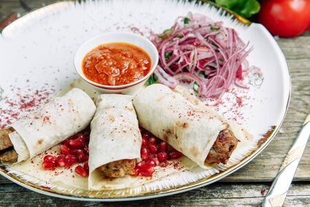 Restaurant dish on a wooden background with vegetables. Lula kebab in lavash with pomegranate and onion on a plate.の写真素材