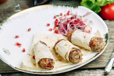 Restaurant dish on a wooden background with vegetables. Lula kebab in lavash with pomegranate and onion on a plate.の写真素材