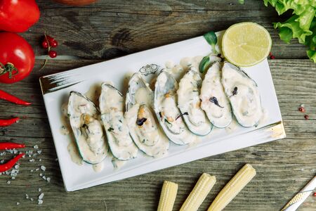 Restaurant dish on a wooden background with vegetables. Mussels in sour cream sauce on a plate with...