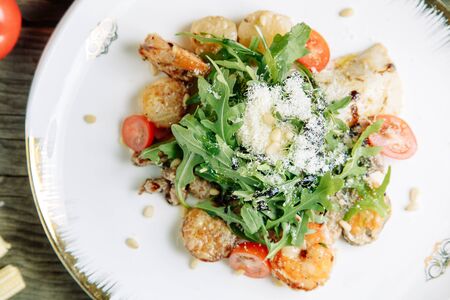 Restaurant dish on a wooden background with vegetables. Salad with shrimp, avocado and arugula on a plate.の写真素材