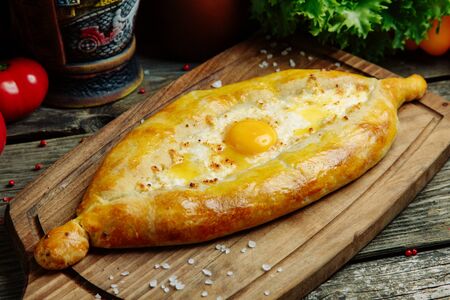 Azerbaijani restaurant dish with vegetable decor on a wooden background. Khachapuri in Adjarian on the Board.の写真素材