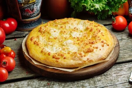 Azerbaijani restaurant dish with vegetable decor on a wooden background. Khachapuri in Megrelian on the Board.の写真素材